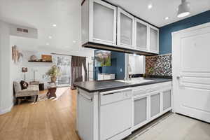 Kitchen featuring decorative backsplash, white dishwasher, sink, light hardwood / wood-style flooring, and white cabinetry