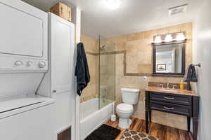 Full bathroom featuring vanity, tiled shower / bath, toilet, stacked washing maching and dryer, and wood-type flooring