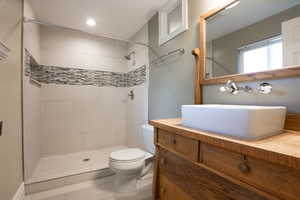 Bathroom featuring a tile shower, tile patterned flooring, vanity, and toilet