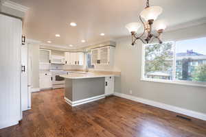 Kitchen featuring white cabinetry, hanging light fixtures, dark hardwood / wood-style floors, kitchen peninsula, and white appliances