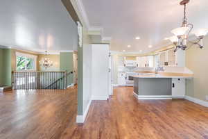 Kitchen with white appliances, crown molding, kitchen peninsula, hardwood / wood-style flooring, and white cabinetry