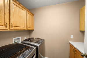 Clothes washing area featuring cabinets, separate washer and dryer, and a textured ceiling