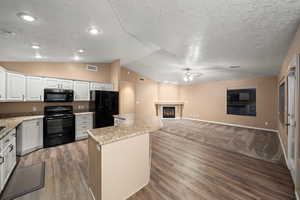 Kitchen featuring vaulted ceiling, a kitchen island, black appliances, wood-type flooring, and white cabinetry