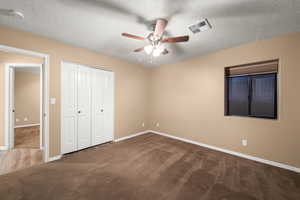 Unfurnished bedroom featuring ceiling fan, a closet, carpet, and a textured ceiling