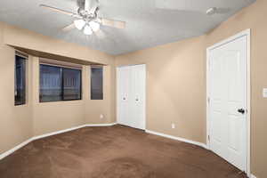 Unfurnished bedroom featuring dark colored carpet, ceiling fan, a textured ceiling, and multiple closets