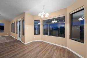 Unfurnished dining area featuring hardwood / wood-style floors, a notable chandelier, and a textured ceiling