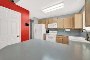 Kitchen featuring light brown cabinets, white appliances, sink, and concrete flooring