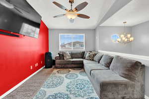 Carpeted living room with ceiling fan with notable chandelier and a textured ceiling