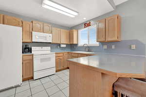 Kitchen featuring white appliances, kitchen peninsula, and light brown cabinetry