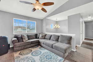 Living room with ceiling fan with notable chandelier, carpet floors, and lofted ceiling