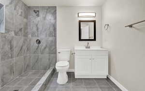 Bathroom featuring tile patterned floors, vanity, toilet, and tiled shower