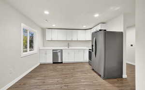 Kitchen with sink, stainless steel appliances, white cabinetry, and light hardwood / wood-style flooring