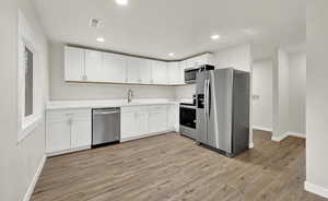 Kitchen featuring light wood-type flooring, stainless steel appliances, white cabinetry, and sink