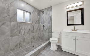 Bathroom with a tile shower, vanity, toilet, and tile patterned floors