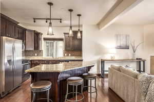 Kitchen featuring pendant lighting, a center island, appliances with stainless steel finishes, dark brown cabinets, and dark hardwood / wood-style flooring