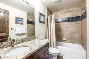 Full bathroom with shower / bathtub combination with curtain, vanity, a textured ceiling, and toilet