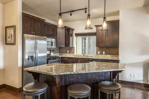 Kitchen featuring decorative backsplash, dark wood-type flooring, hanging light fixtures, and appliances with stainless steel finishes