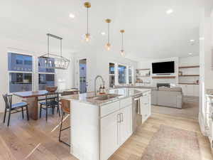 Kitchen with sink, stainless steel dishwasher, an island with sink, decorative light fixtures, and white cabinetry