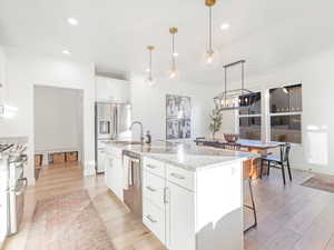 Kitchen with a kitchen island with sink, white cabinets, light hardwood / wood-style floors, and decorative light fixtures