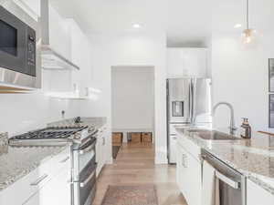 Kitchen with appliances with stainless steel finishes, light stone counters, white cabinetry, and wall chimney range hood