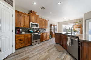 Kitchen with backsplash, sink, dark stone countertops, light hardwood / wood-style floors, and stainless steel appliances