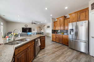 Kitchen featuring light stone countertops, ceiling fan, sink, stainless steel appliances, and light hardwood / wood-style floors