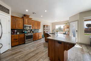 Kitchen with appliances with stainless steel finishes, a center island with sink, and light hardwood / wood-style flooring