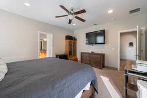 Carpeted bedroom featuring ensuite bath and ceiling fan