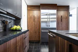 Kitchen featuring stainless steel built in refrigerator, decorative backsplash, and dark tile patterned flooring