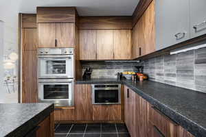 Kitchen with dark tile patterned flooring, stainless steel double oven, and tasteful backsplash