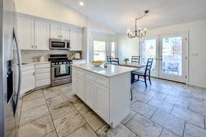 Kitchen featuring white cabinets, appliances with stainless steel finishes, decorative light fixtures, and lofted ceiling