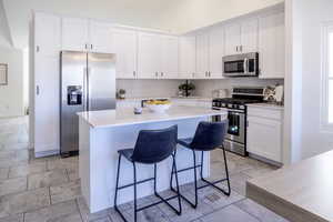 Kitchen featuring a kitchen bar, appliances with stainless steel finishes, white cabinetry, and a kitchen island