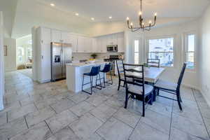 Kitchen with white cabinetry, a center island, stainless steel appliances, lofted ceiling, and decorative light fixtures