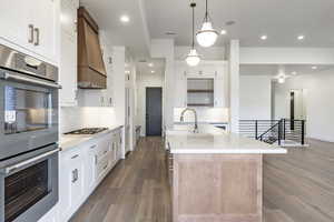 Kitchen with white cabinetry, sink, premium range hood, hardwood / wood-style flooring, and appliances with stainless steel finishes