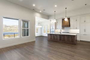 Kitchen featuring a center island with sink, white cabinets, tasteful backsplash, dark hardwood / wood-style flooring, and custom range hood