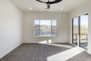 Carpeted spare room featuring ceiling fan, a water and mountain view, and a healthy amount of sunlight