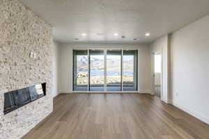 Unfurnished living room with a textured ceiling, hardwood / wood-style flooring, and a stone fireplace