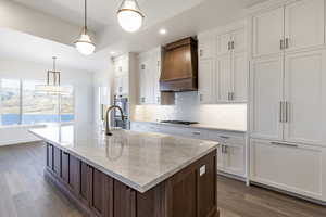 Kitchen featuring appliances with stainless steel finishes, custom range hood, pendant lighting, dark hardwood / wood-style floors, and white cabinetry