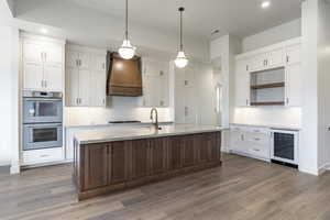 Kitchen featuring custom range hood, stainless steel double oven, sink, dark hardwood / wood-style floors, and wine cooler