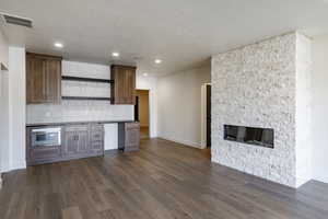 Kitchen with decorative backsplash, a fireplace, dark wood-type flooring, and stainless steel oven