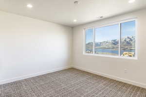 Carpeted spare room featuring a textured ceiling and a water and mountain view