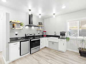 Kitchen with light wood-type flooring, stainless steel appliances, sink, wall chimney range hood, and white cabinets