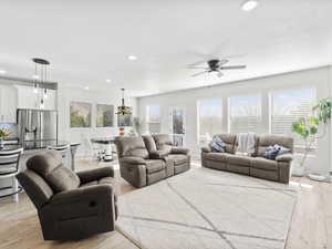 Family room featuring ceiling fan with notable chandelier, light wood-type flooring, and a healthy amount of sunlight