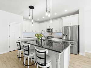 Kitchen with white cabinets, light wood-type flooring, stainless steel appliances, and a kitchen island with sink