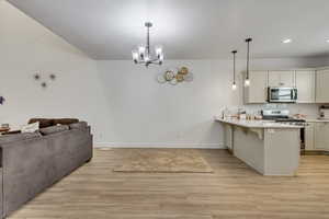 Kitchen featuring kitchen peninsula, appliances with stainless steel finishes, decorative light fixtures, and a breakfast bar area