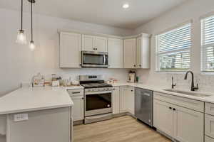 Kitchen featuring sink, kitchen peninsula, decorative light fixtures, white cabinets, and appliances with stainless steel finishes