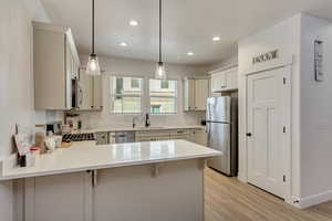 Kitchen with hanging light fixtures, light hardwood / wood-style flooring, appliances with stainless steel finishes, a kitchen bar, and kitchen peninsula