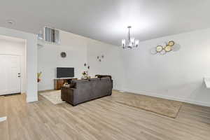 Living room with light hardwood / wood-style floors, a textured ceiling, and an inviting chandelier