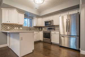 Kitchen with dark wood-type flooring, white cabinets, a textured ceiling, appliances with stainless steel finishes, and tasteful backsplash