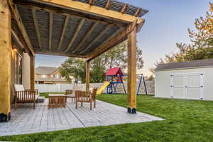 Patio terrace at dusk featuring an outdoor living space, a shed, a playground, and a yard